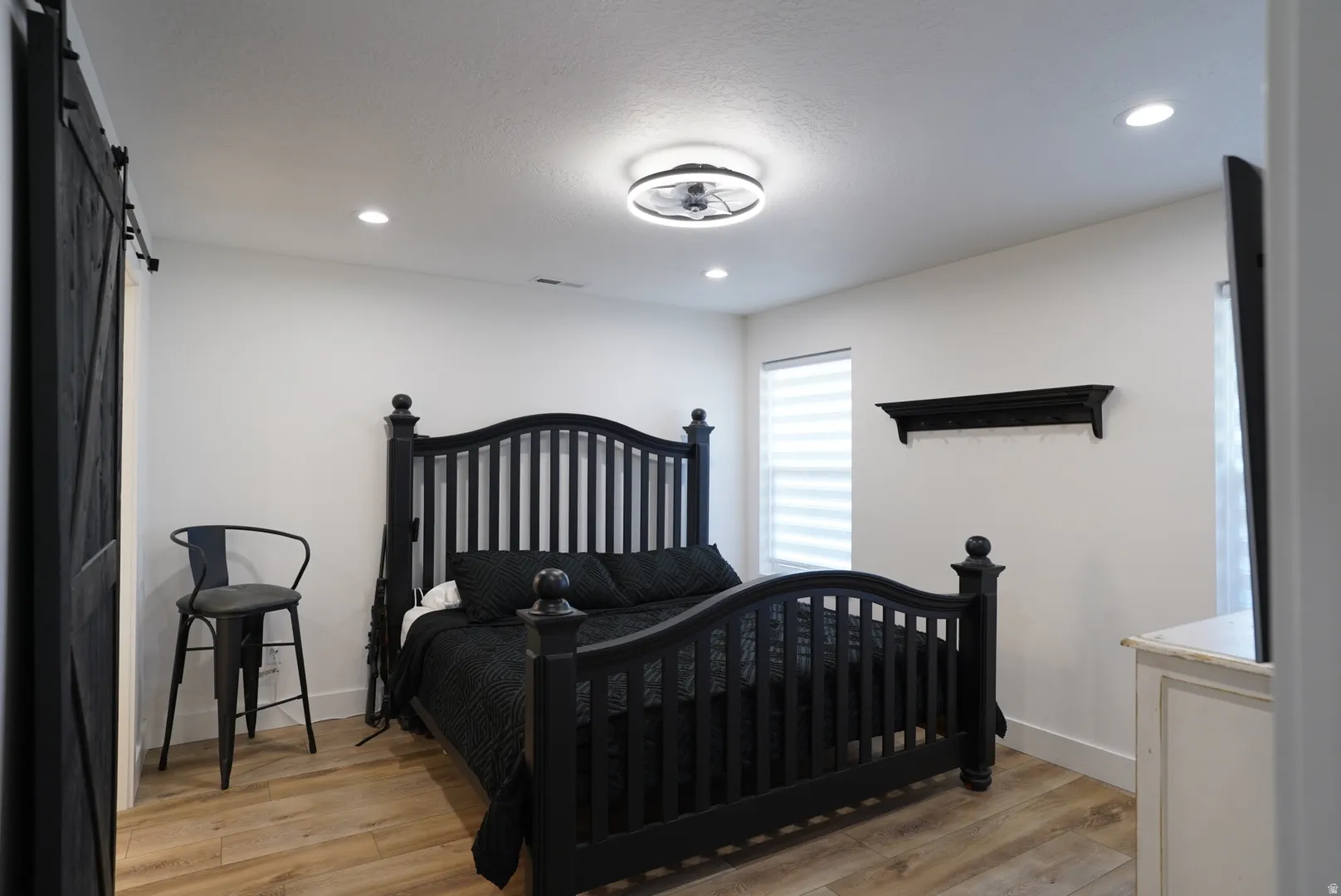 Bedroom with a barn door, light wood-type flooring, recessed lighting, and a textured ceiling