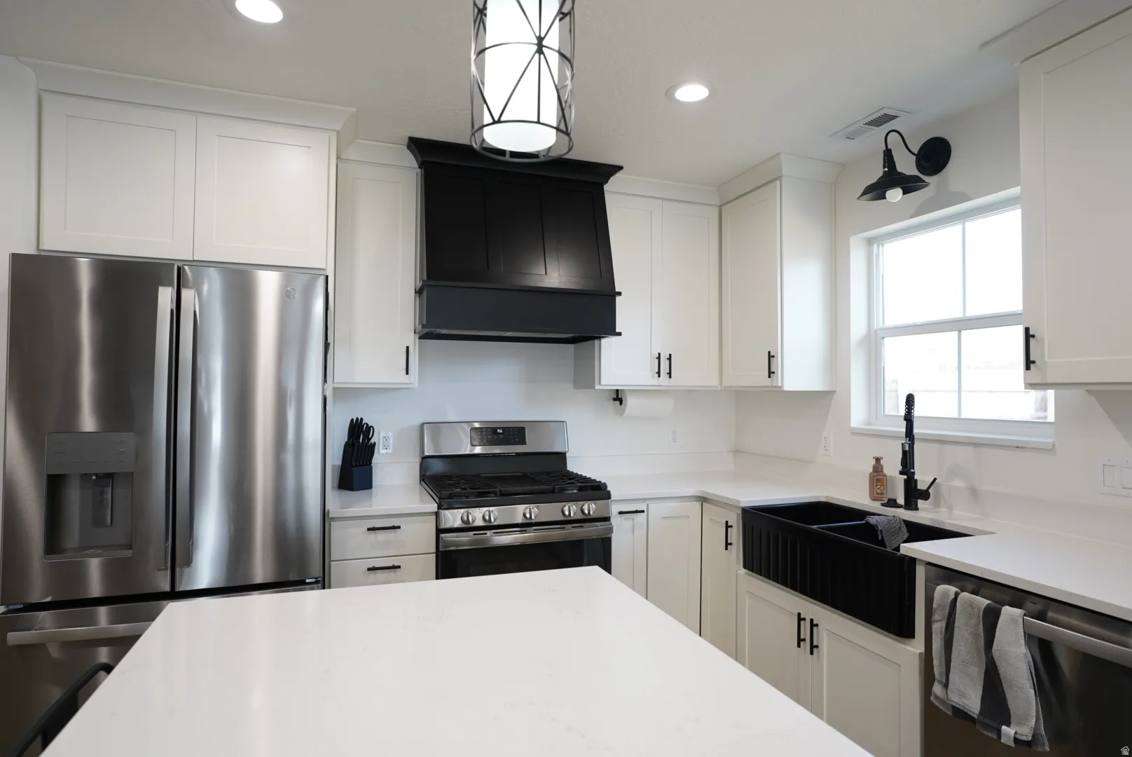 Kitchen with appliances with stainless steel finishes, white cabinetry, recessed lighting, custom exhaust hood, and light stone counters