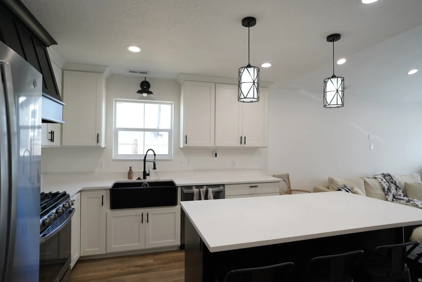 Kitchen with stainless steel appliances, white cabinets, decorative light fixtures, dark wood finished floors, and a kitchen breakfast bar