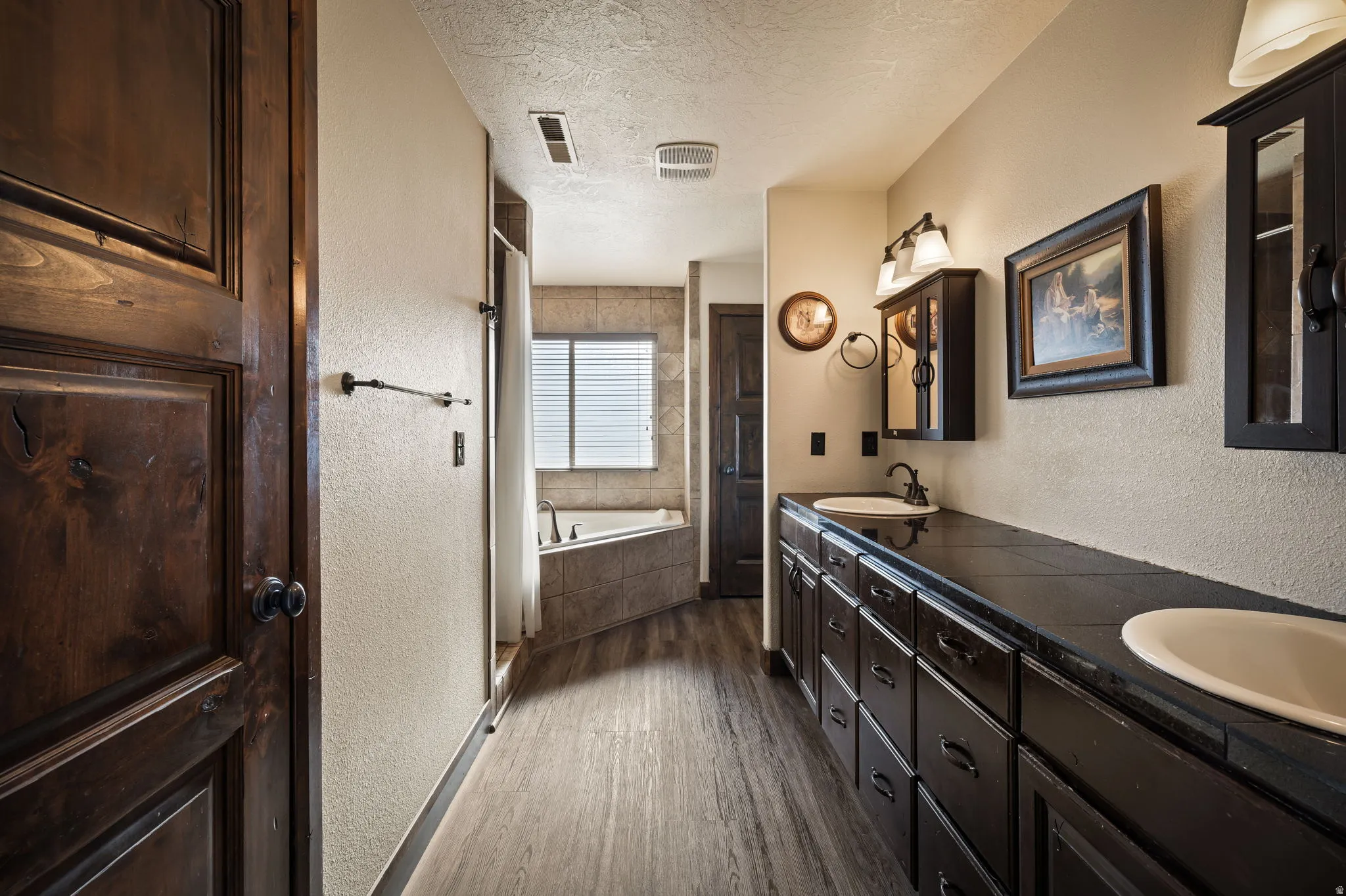 Master Bathroom with a textured wall, dark wood-style flooring, a textured ceiling, double vanity, and a garden tub