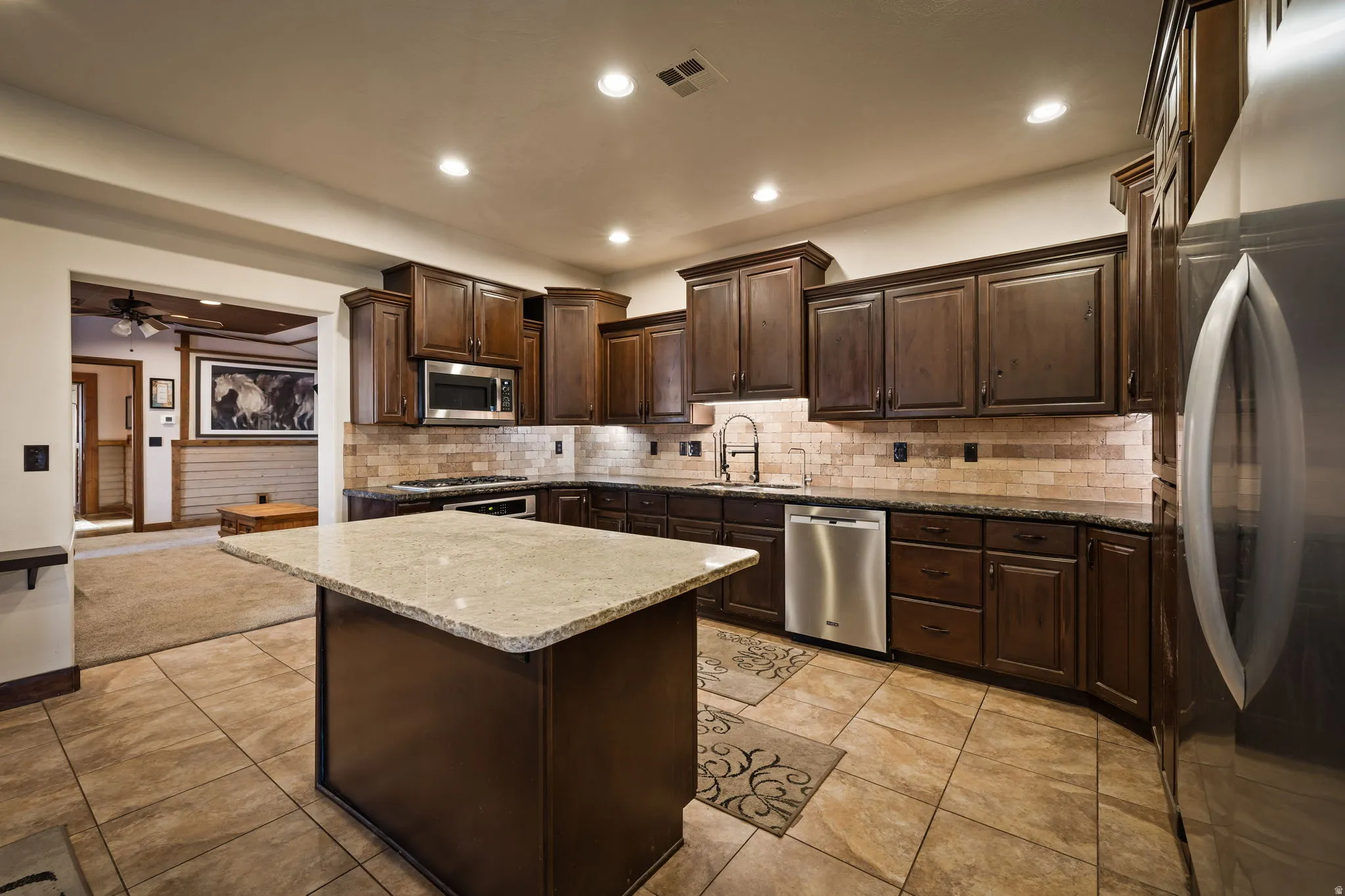 Kitchen with dark brown cabinets, appliances with stainless steel finishes, a kitchen island, light stone countertops, and a ceiling fan