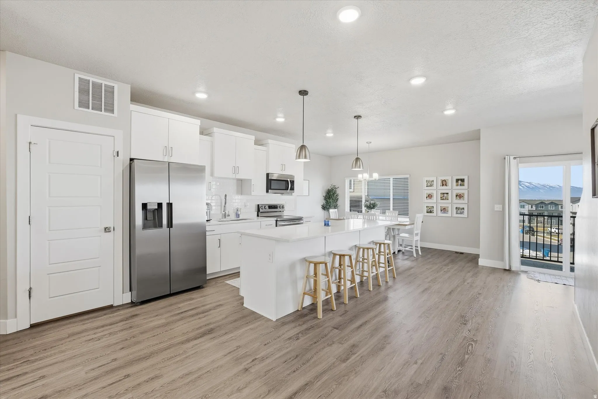 Kitchen with hanging light fixtures, stainless steel appliances, a center island with sink, white cabinets, and a breakfast bar