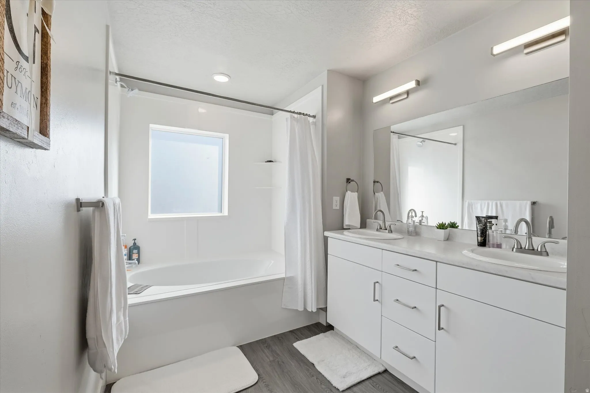 Bathroom with shower / tub combo with curtain, double vanity, a textured ceiling, and dark wood-style flooring