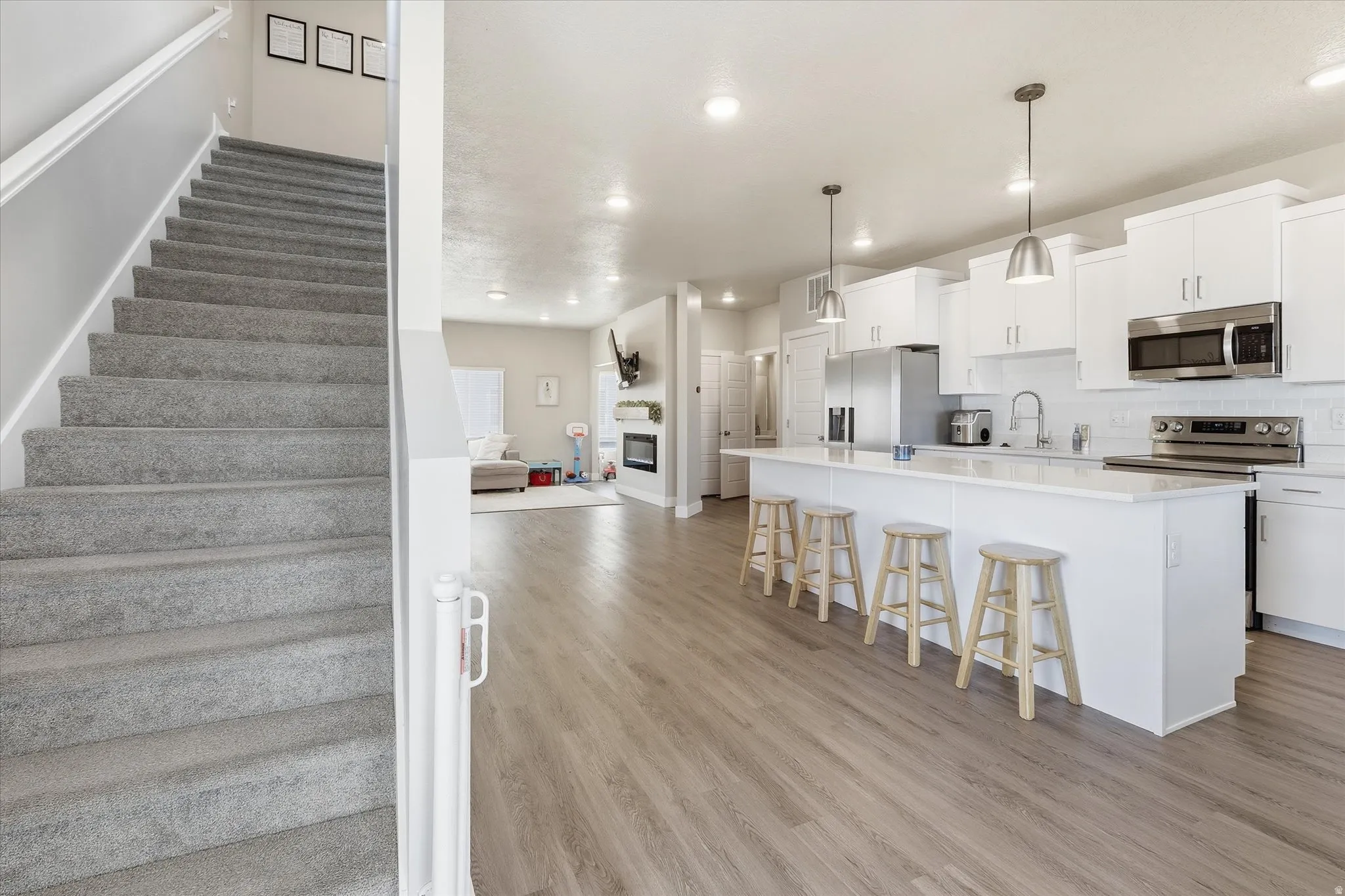 Kitchen with a kitchen breakfast bar, an island with sink, white cabinetry, a glass covered fireplace, and appliances with stainless steel finishes