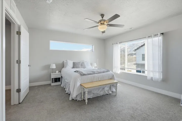 Bedroom with a textured ceiling, light carpet, and ceiling fan