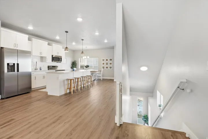 Kitchen featuring appliances with stainless steel finishes, white cabinets, hanging light fixtures, light wood-style flooring, and a breakfast bar