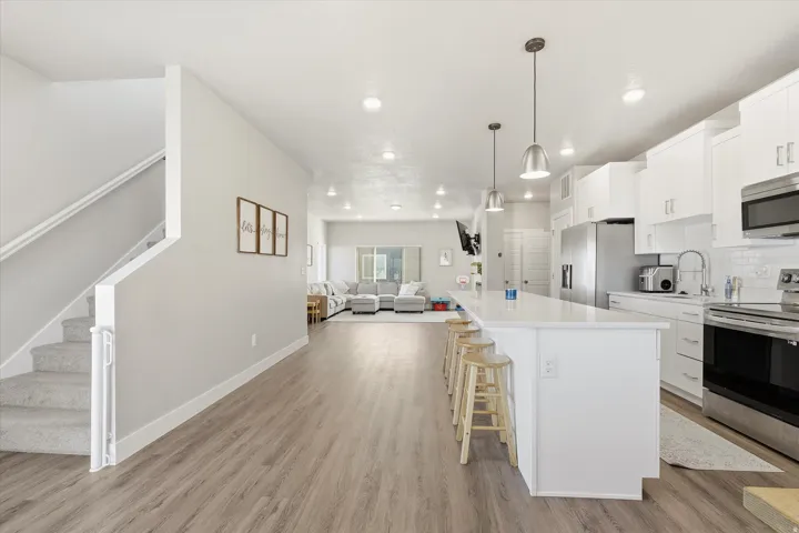 Kitchen with white cabinets, open floor plan, stainless steel appliances, hanging light fixtures, and a breakfast bar