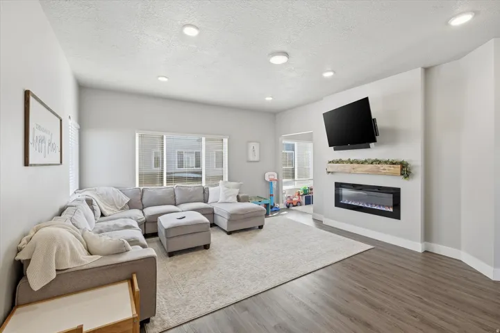 Living room with a textured ceiling, a glass covered fireplace, wood finished floors, and recessed lighting
