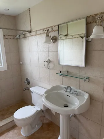 Bathroom featuring a pedestal sink, chrome faucet, wall-mounted mirror, and tile-surround shower with a window