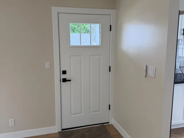 Entryway featuring a white paneled door with window pane, matte black hardware, and wood-finish flooring