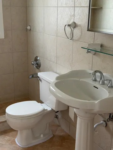 Bathroom featuring a pedestal sink, white toilet, and polished chrome fixtures