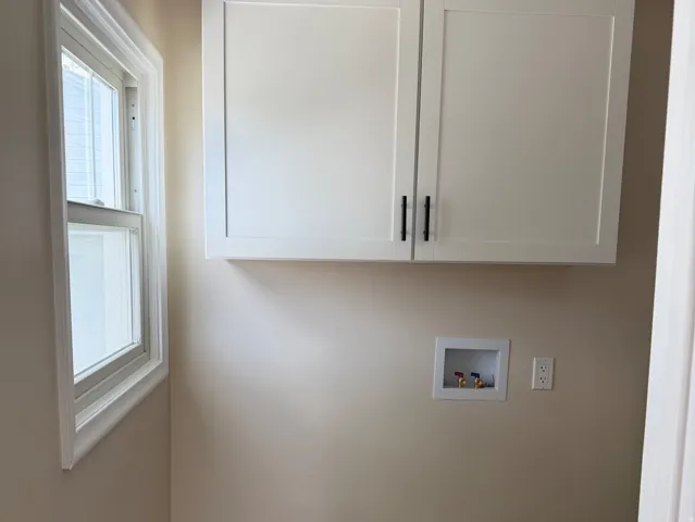 Utility space featuring two white shaker-style upper cabinets with black hardware, wood-finish flooring, and a single window with white trim