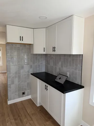 Corner cabinetry with white shaker-style doors and matte black hardware, complemented by a black countertop