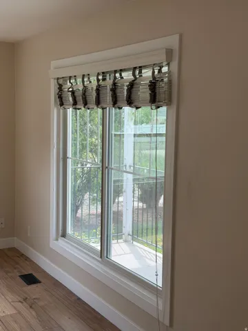 Large window with white trim, featuring a custom roman shade and wood-finish flooring