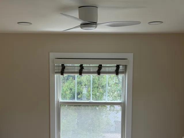 Room featuring wood-finish flooring, a window with a fabric Roman shade, and a ceiling fan with integrated lighting
