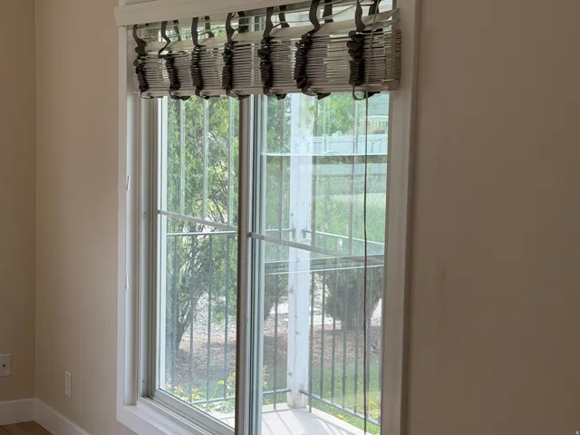 Large window with white trim, featuring a custom roman shade and wood-finish flooring