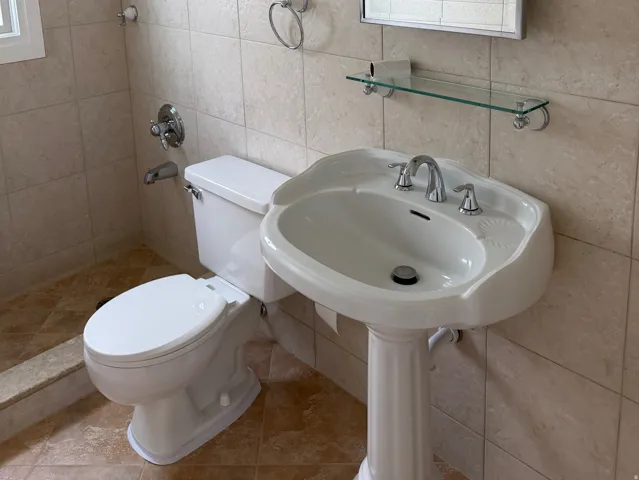 Bathroom featuring a pedestal sink, chrome faucet, wall-mounted mirror, and tile-surround shower with a window