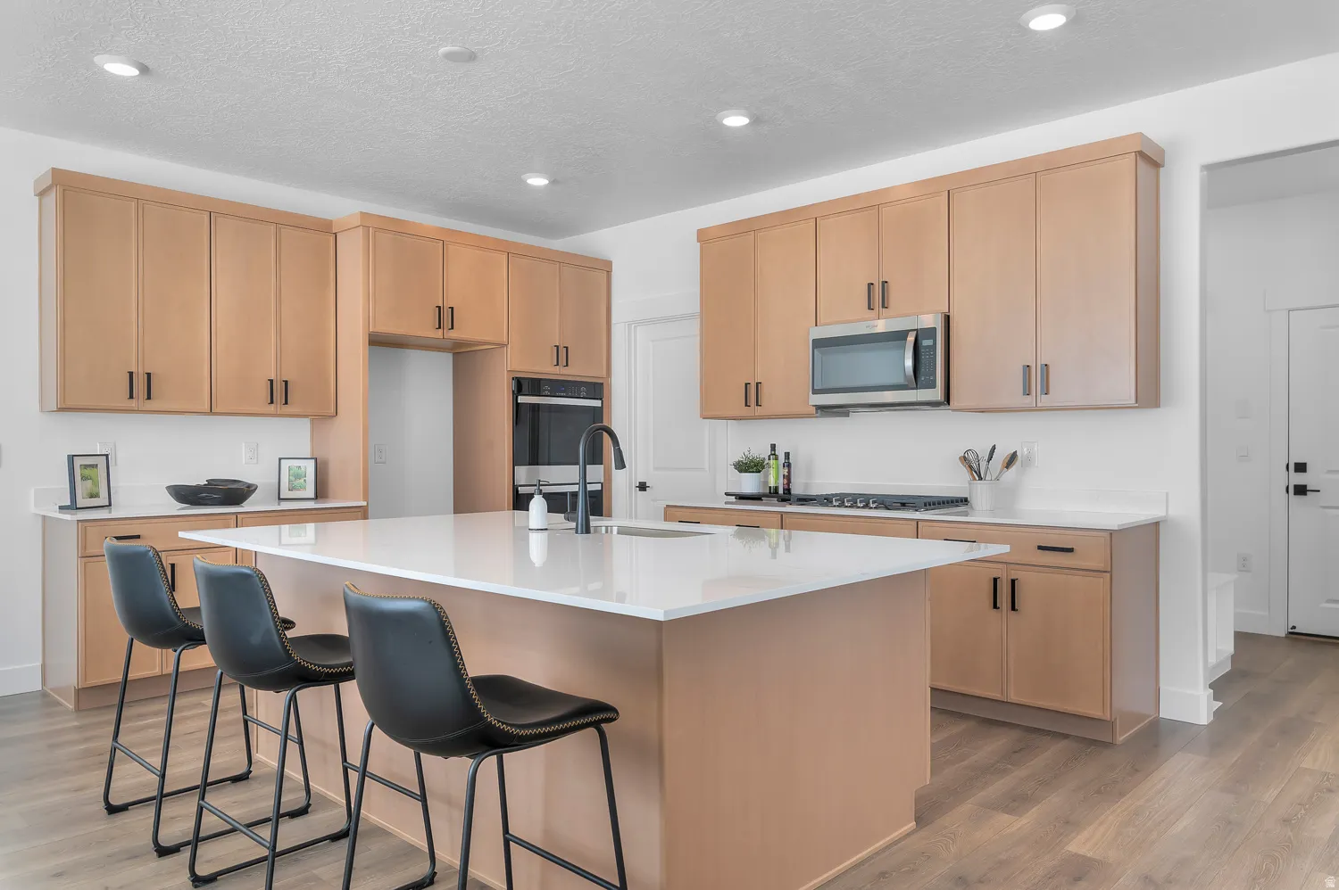 Kitchen with light wood-style flooring, a breakfast bar, a kitchen island with sink, light wood finish cabinets, and stainless steel appliances