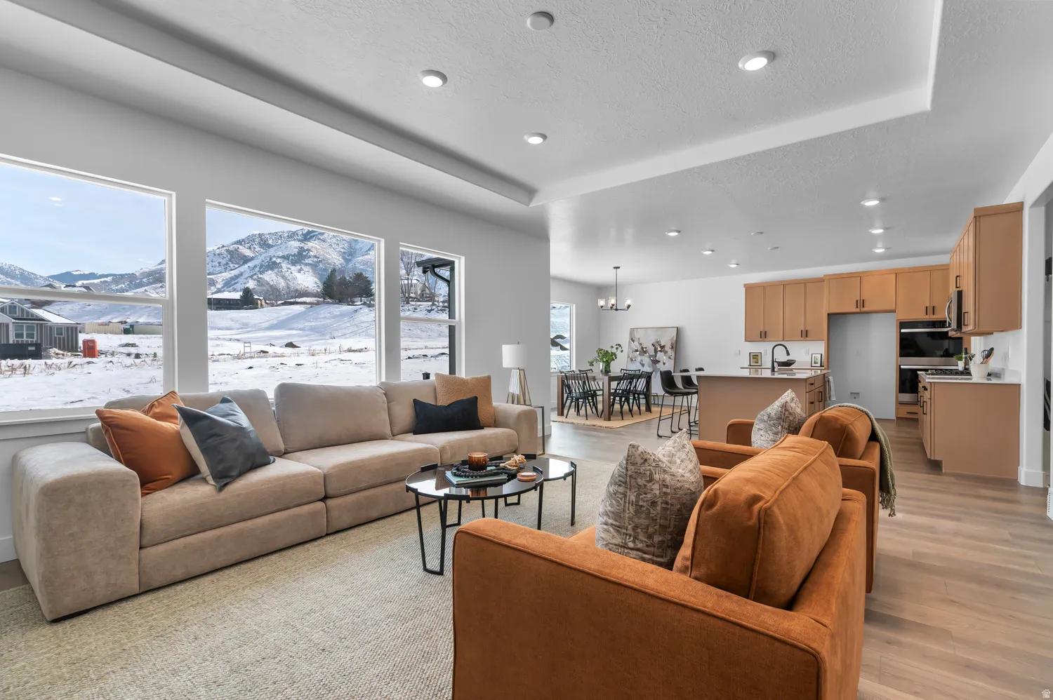 Living area with a mountain view, a textured ceiling, light wood-style floors, hanging lights, and a raised ceiling
