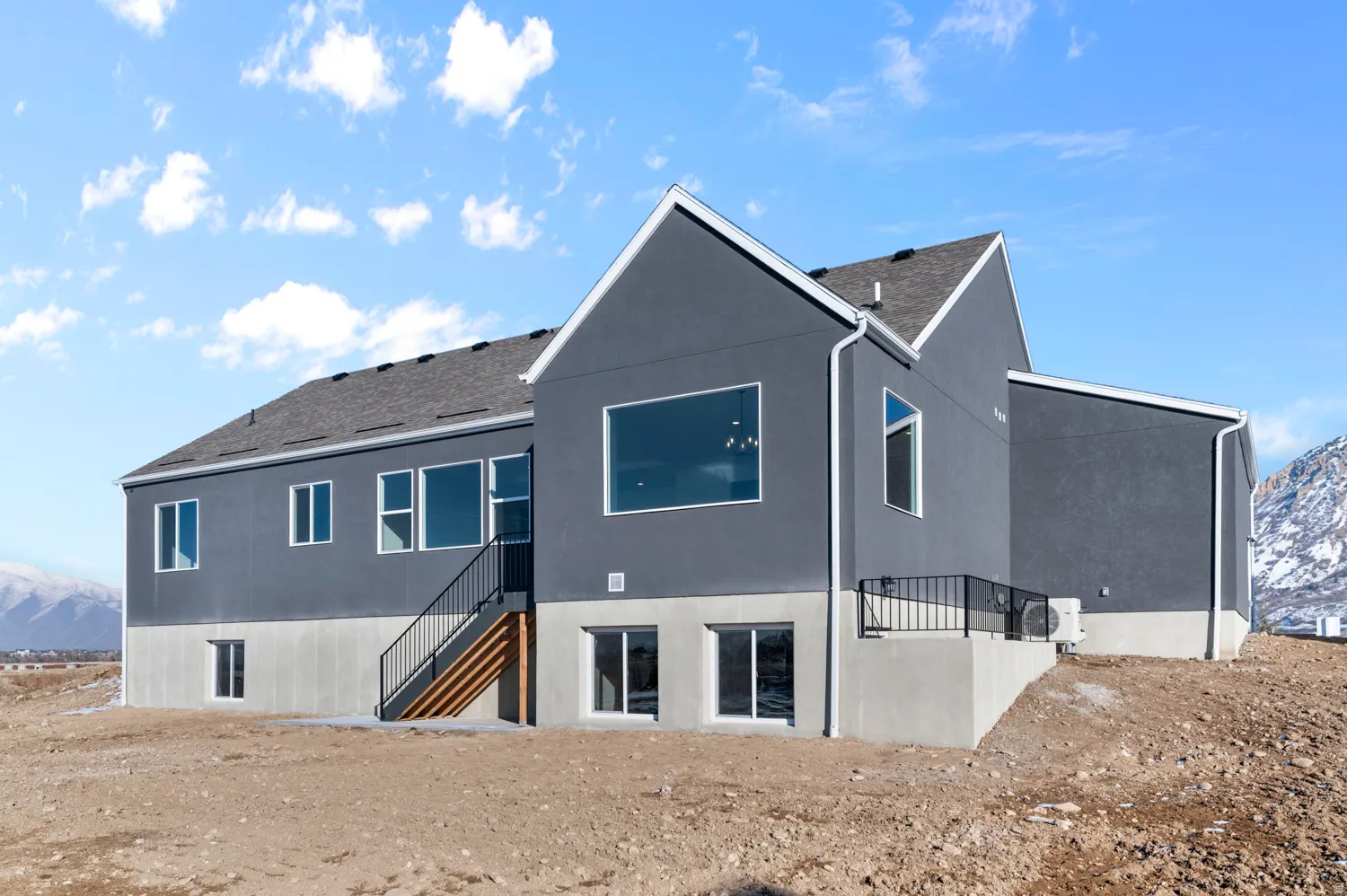 Back of property featuring a mountain view, stairs, a shingled roof, and stucco siding
