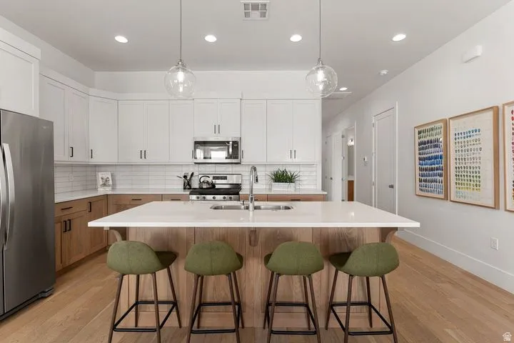 Kitchen with white cabinets, appliances with stainless steel finishes, pendant lighting, light wood-style flooring, and recessed lighting