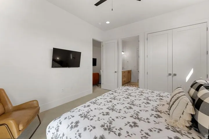 Bedroom with light colored carpet, a closet, a ceiling fan, and ensuite bath