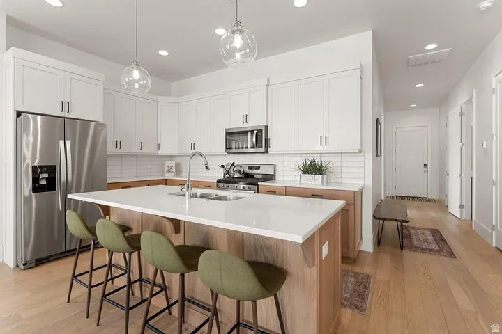 Kitchen with stainless steel appliances, white cabinets, light wood-style floors, pendant lighting, and recessed lighting