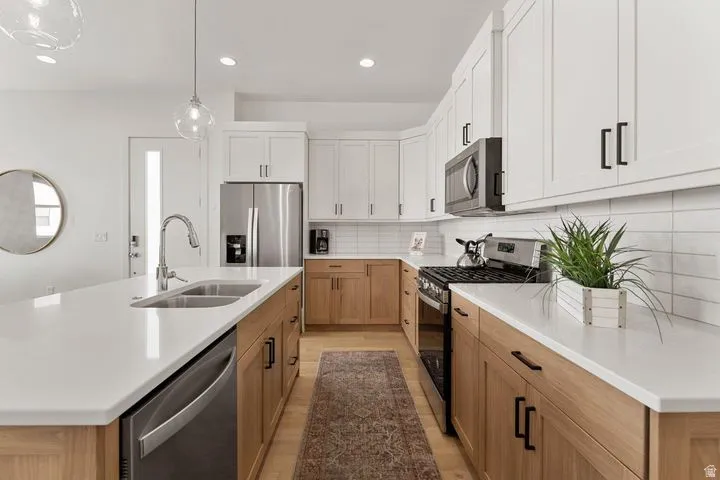 Kitchen with stainless steel appliances, hanging light fixtures, a center island with sink, white cabinetry, and recessed lighting