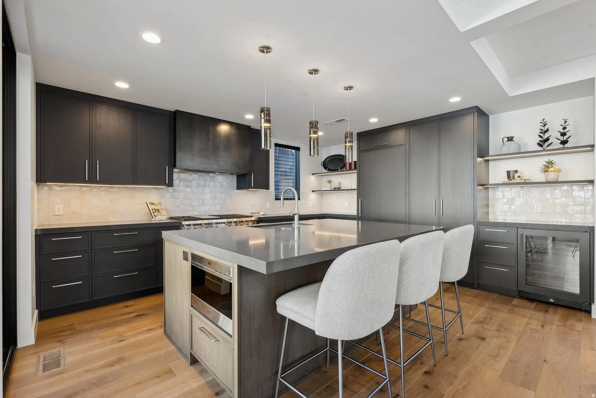 Kitchen featuring open shelves, an island with sink, pendant lighting, wine cooler, and backsplash