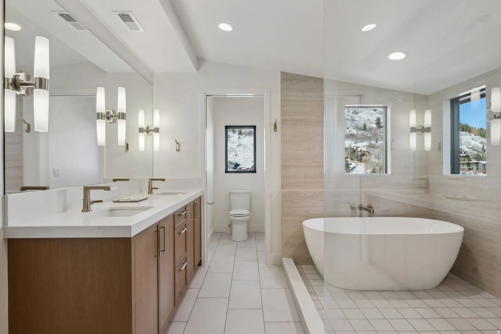 Full bathroom featuring vaulted ceiling, a freestanding bath, double vanity, light tile patterned floors, and recessed lighting