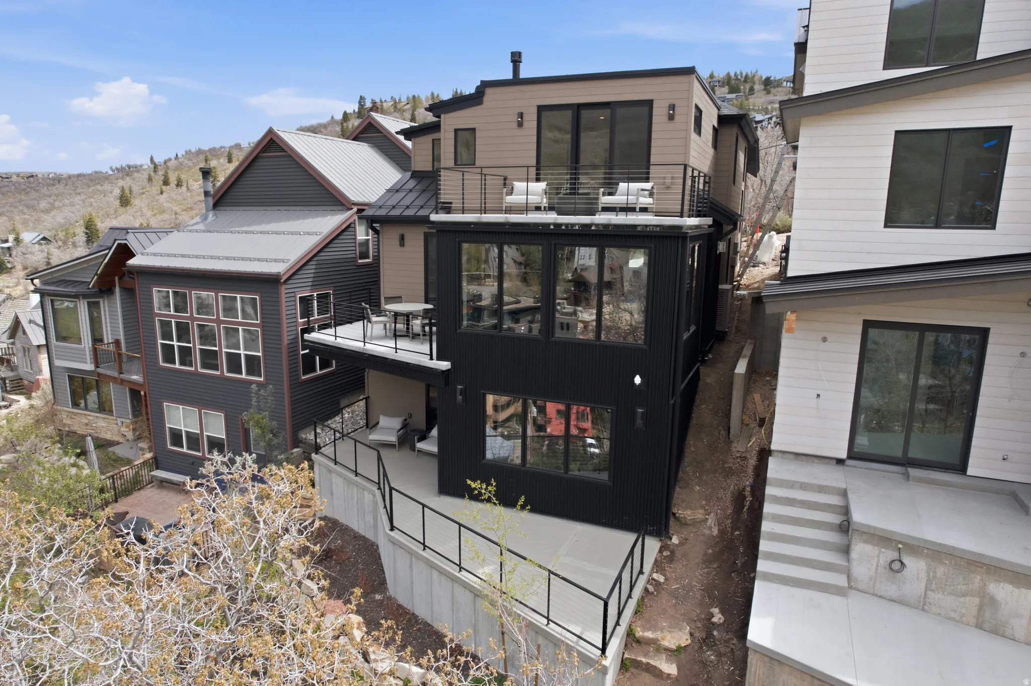 Contemporary multi-level residence featuring dark siding, multiple balconies with metal railings, extensive glazing, and a metal roof
