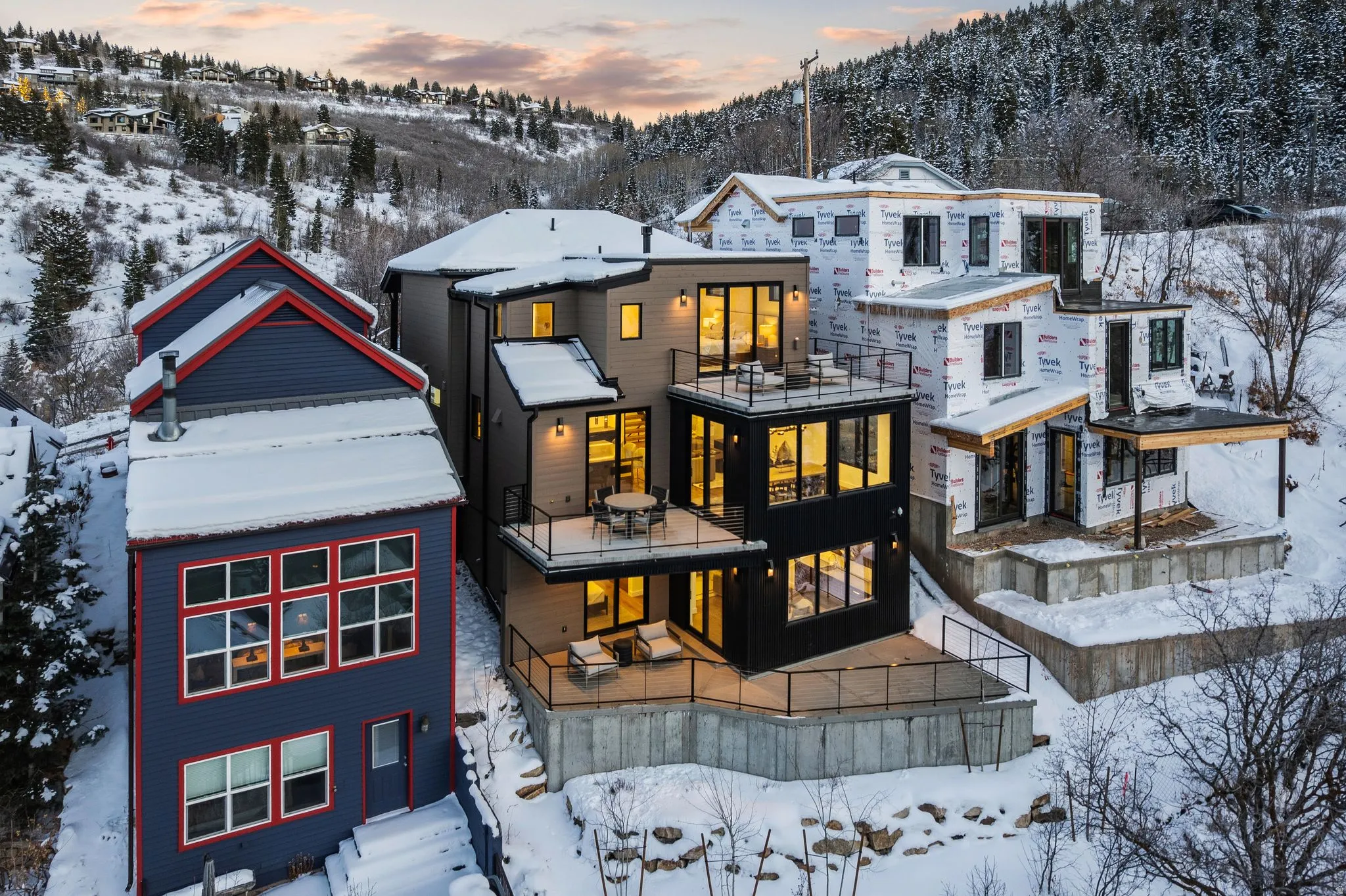 Snow covered rear of property with a balcony, a mountain view, and view of wooded area