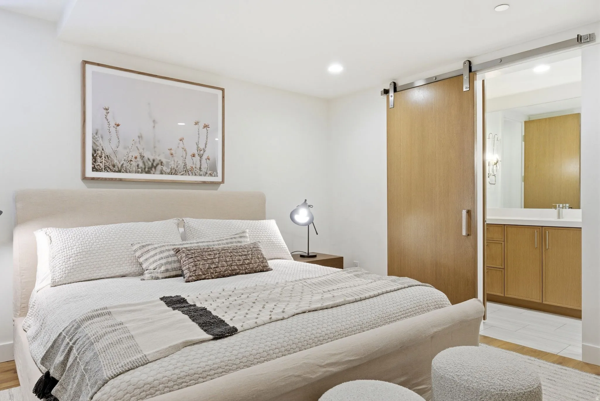 Bedroom with light wood-style floors, a barn door, connected bathroom, and recessed lighting