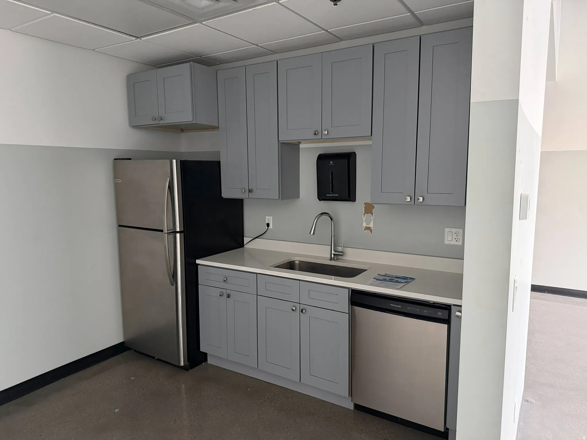 Kitchen featuring gray cabinetry, stainless steel appliances, a paneled ceiling, finished concrete flooring, and light stone countertops