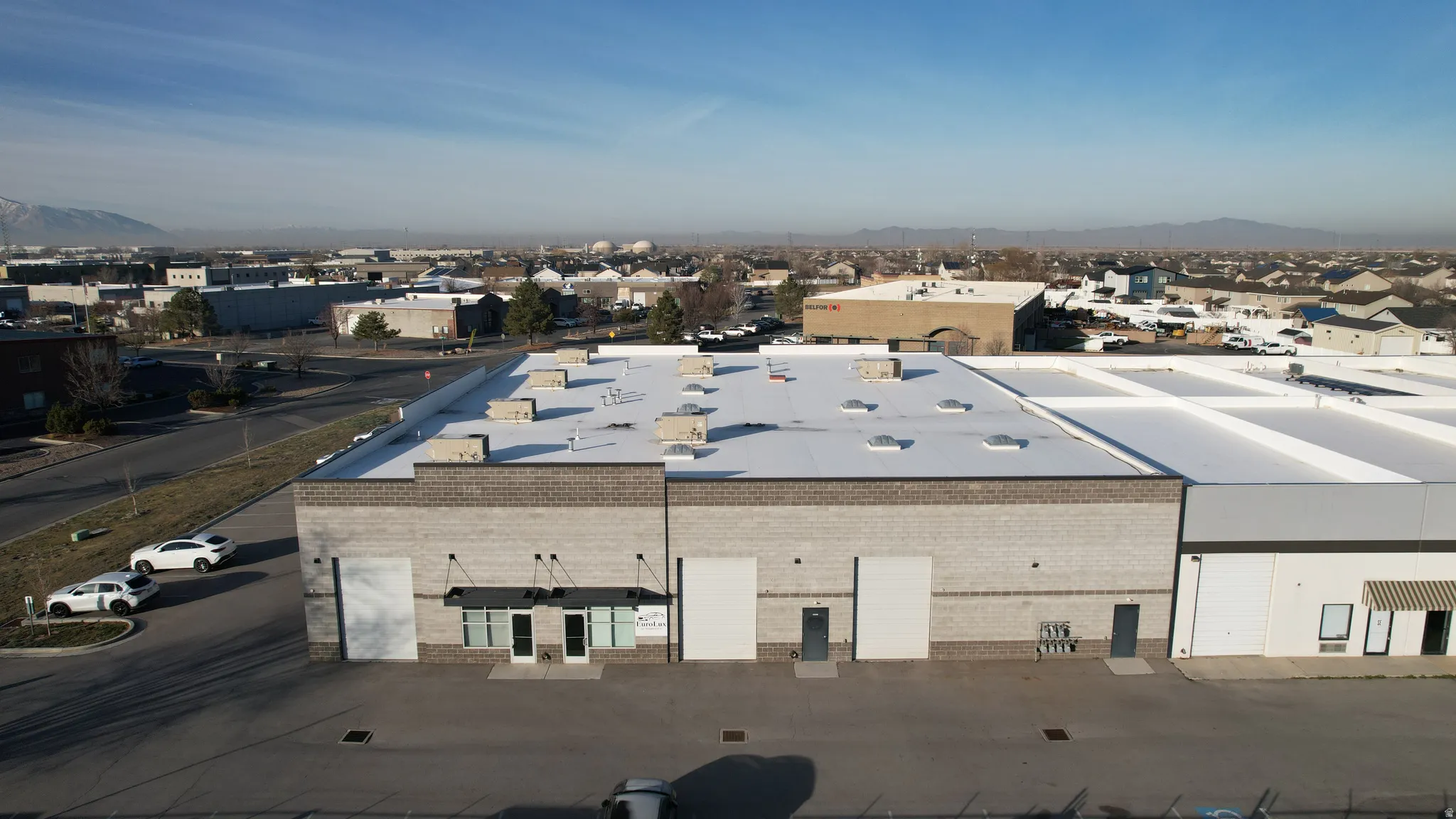 Commercial building featuring a brick facade, multiple entry points, a large parking lot, and a flat roof with visible HVAC units