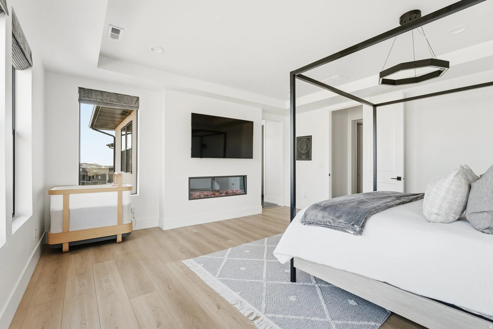 Bedroom featuring light wood finished floors, a glass covered fireplace, recessed lighting, and a raised ceiling