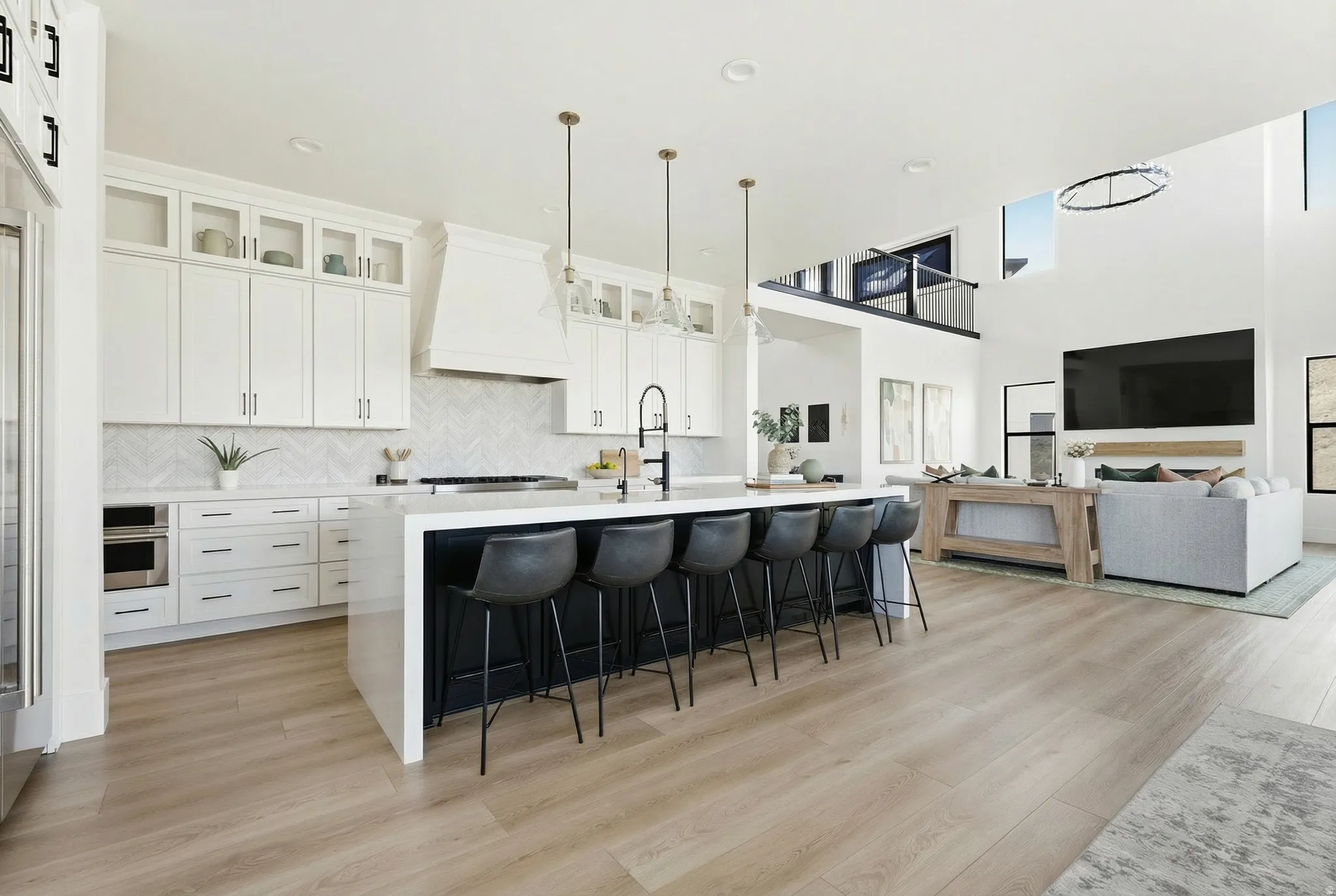 Kitchen featuring a kitchen bar, white cabinets, an island with sink, pendant lighting, and glass insert cabinets - Digitally Staged