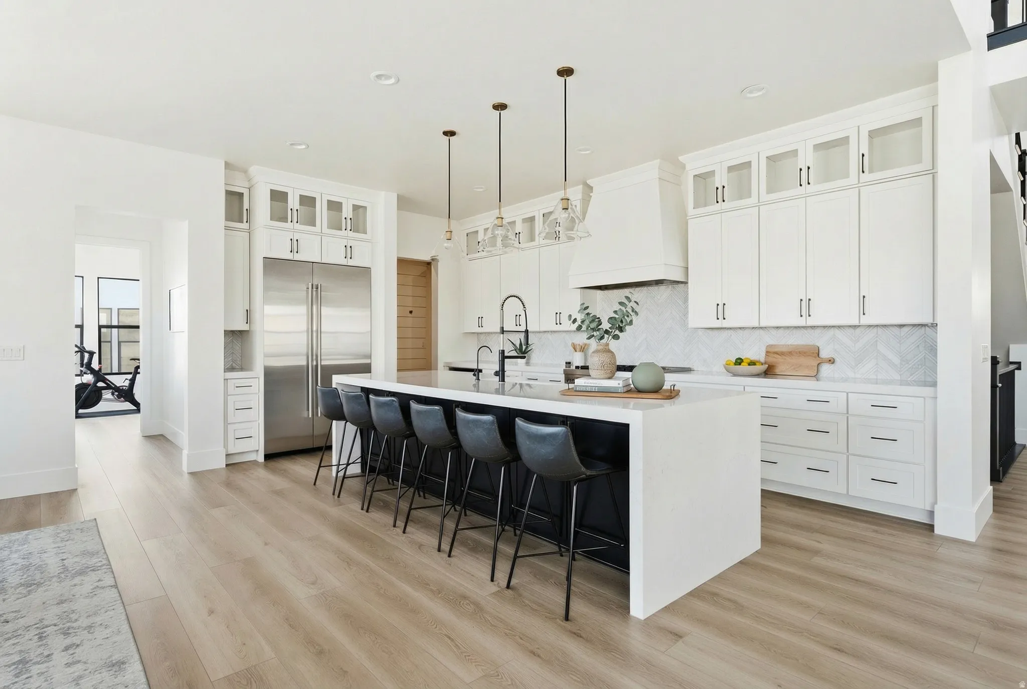 Kitchen with a kitchen breakfast bar, stainless steel built in refrigerator, a kitchen island with sink, glass insert cabinets, and light stone countertops