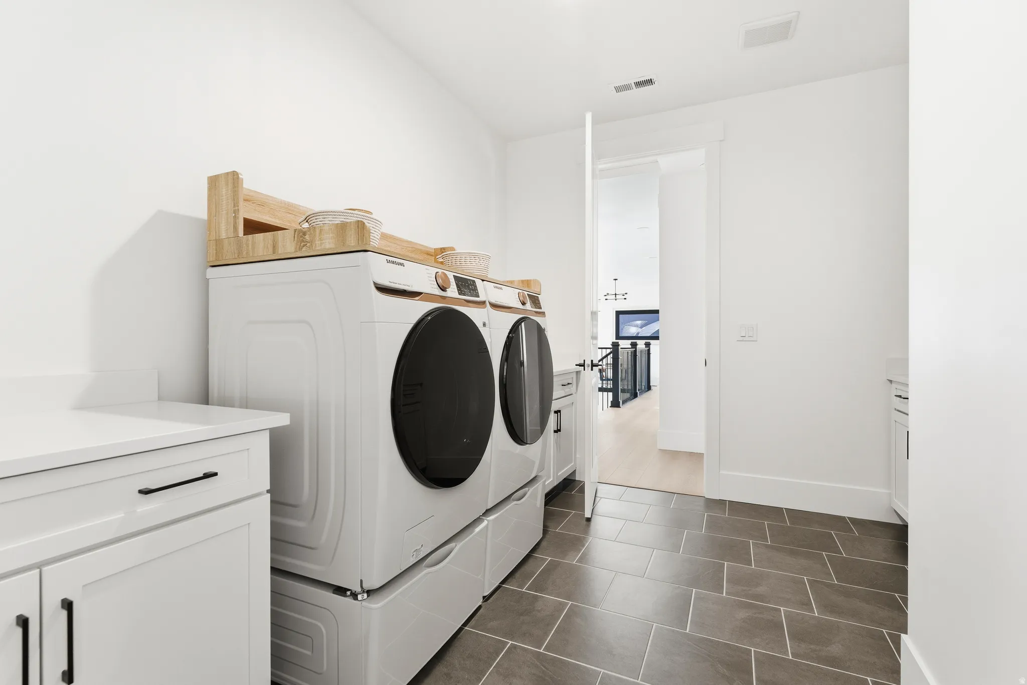 Second floor Washroom that connects to master closet and hallway featuring cabinet space, independent washer and dryer, and dark tile patterned flooring