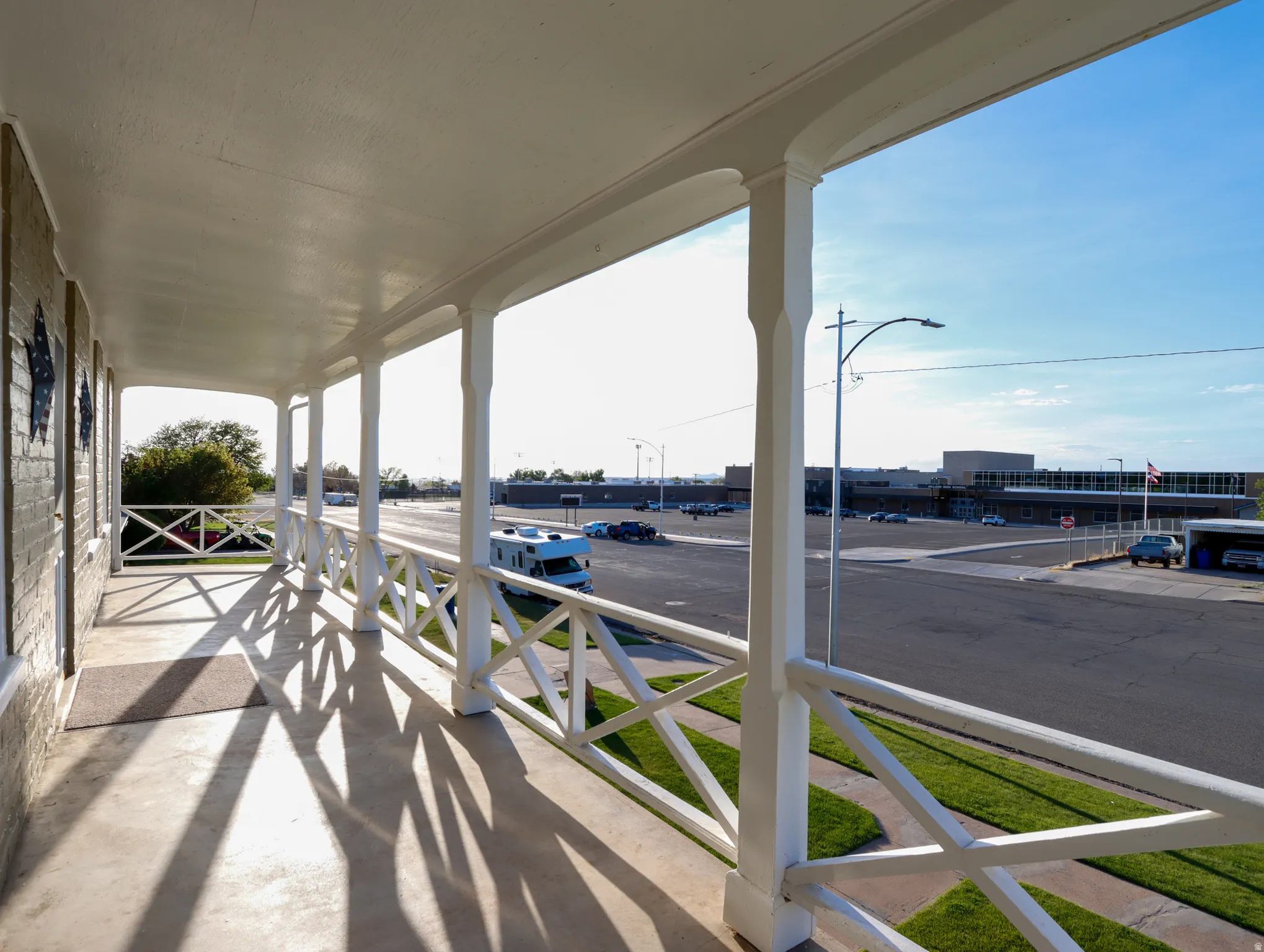 Covered porch with white painted columns and railing, featuring a concrete surface and a brick exterior wall