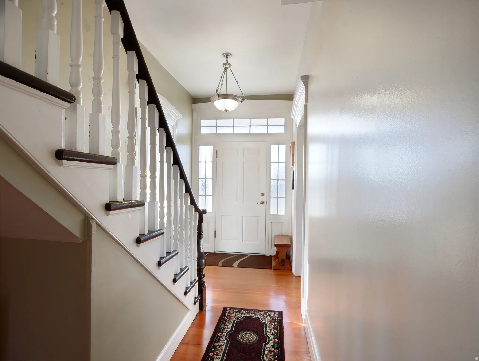 Entryway featuring wood-finish flooring, a white paneled front door with sidelights and transom windows, and a staircase with white balusters and dark wood handrails