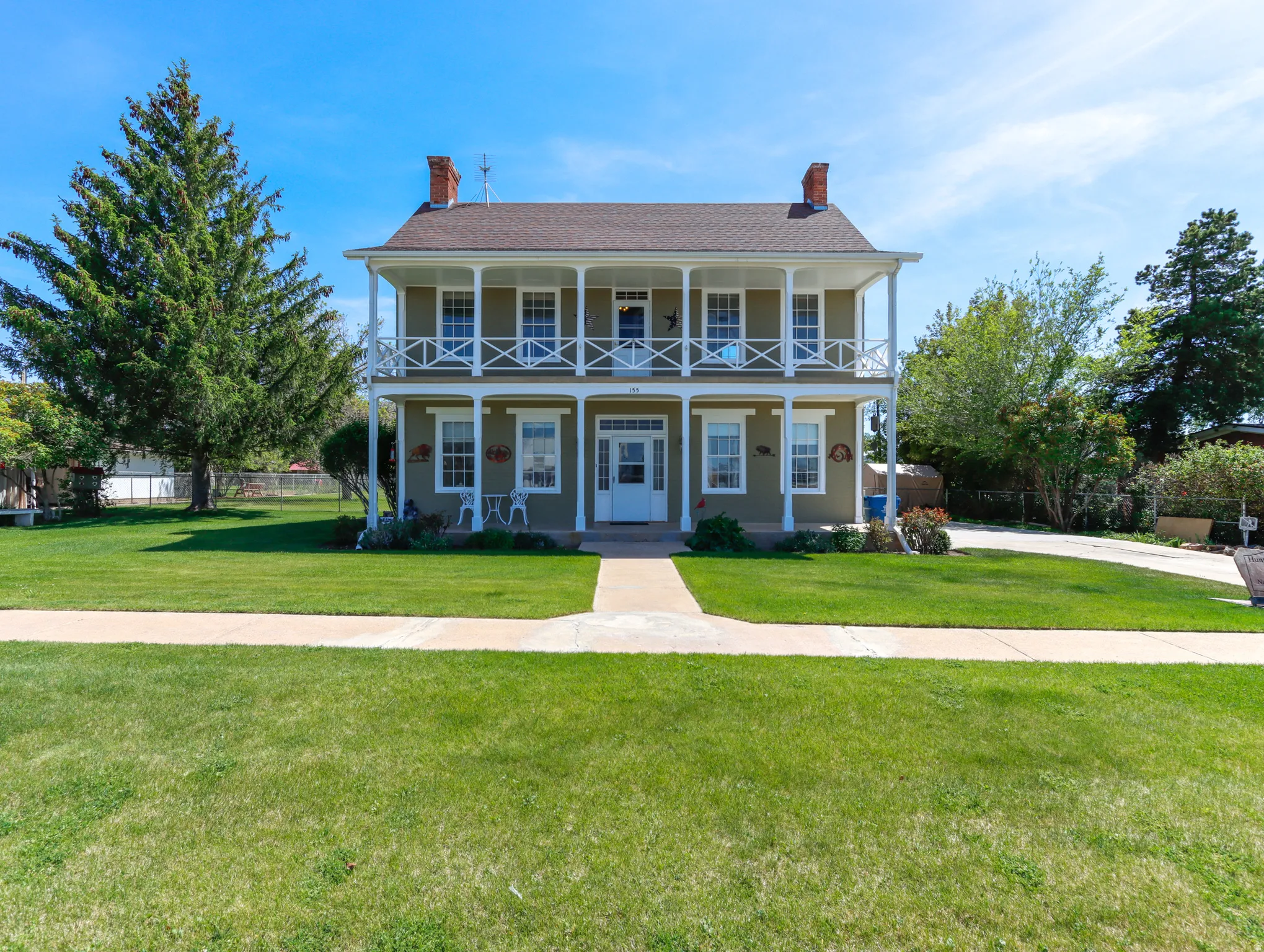Two-story residence featuring a covered double-level porch with white railings, a tan exterior, and a brown shingled roof