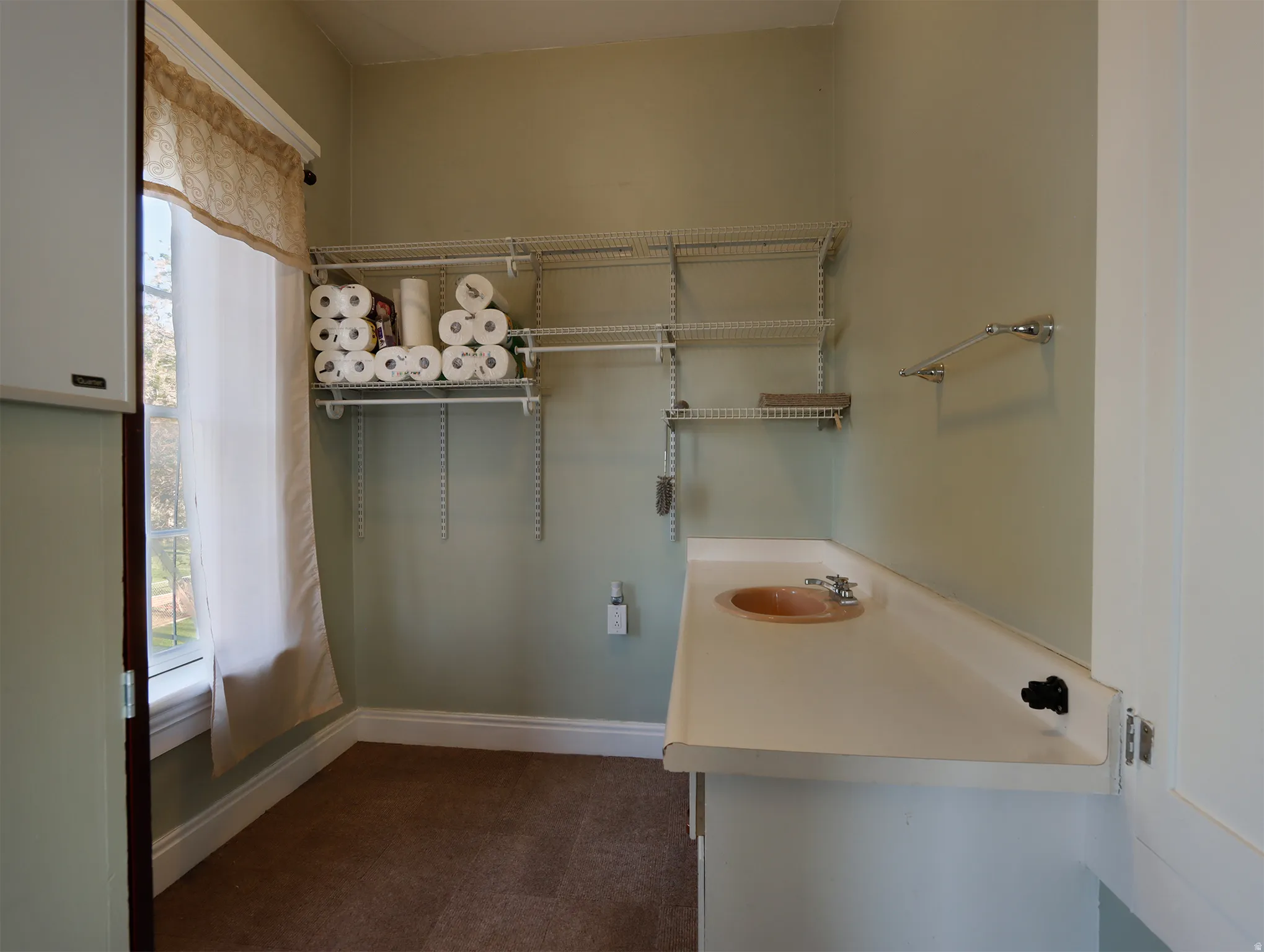 Bathroom featuring a window with a valance, light green painted walls, wire shelving, a towel bar, and a vanity with an integrated sink