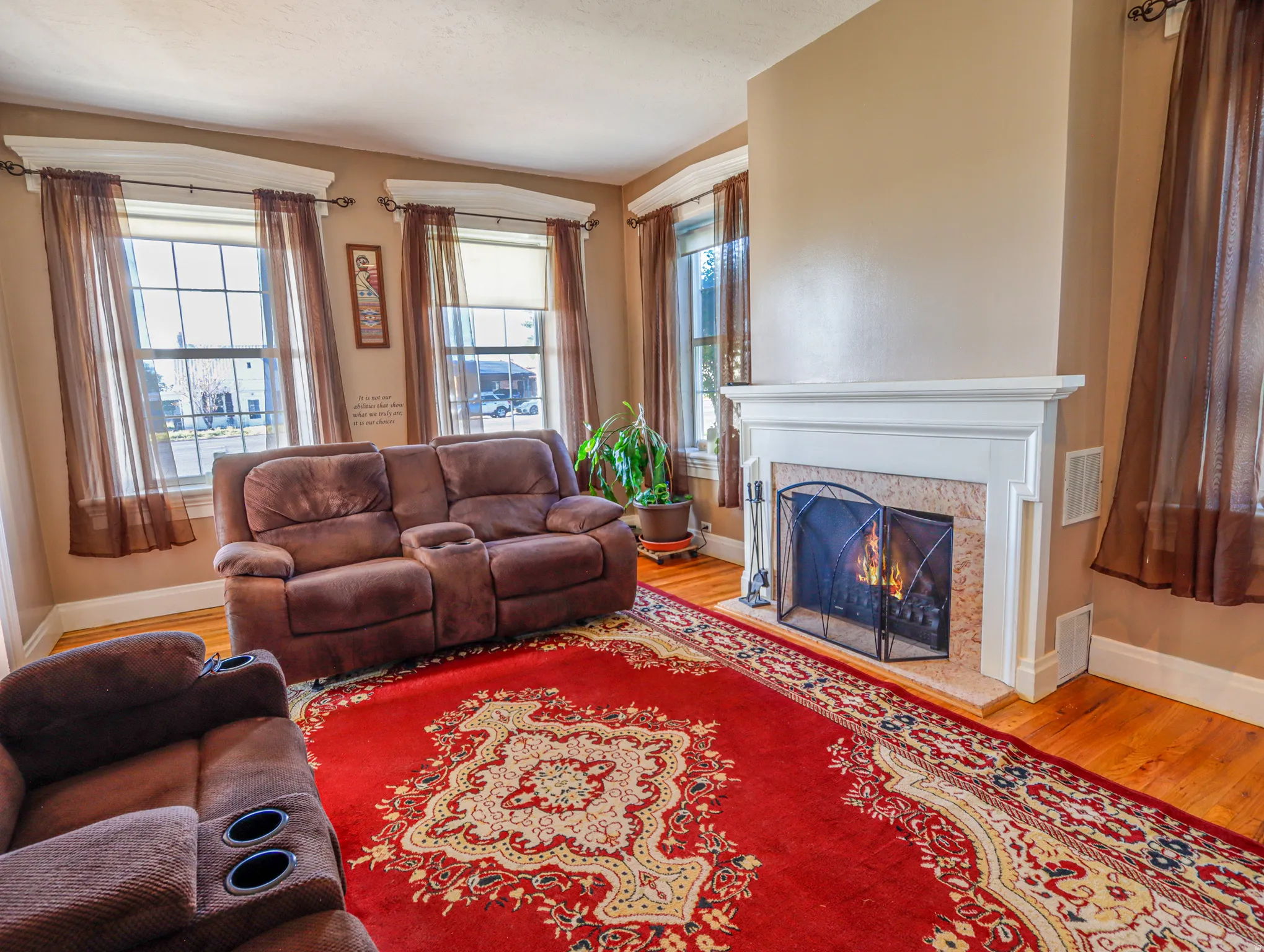 Living area featuring hardwood flooring, a decorative fireplace with a white mantel, and multiple windows