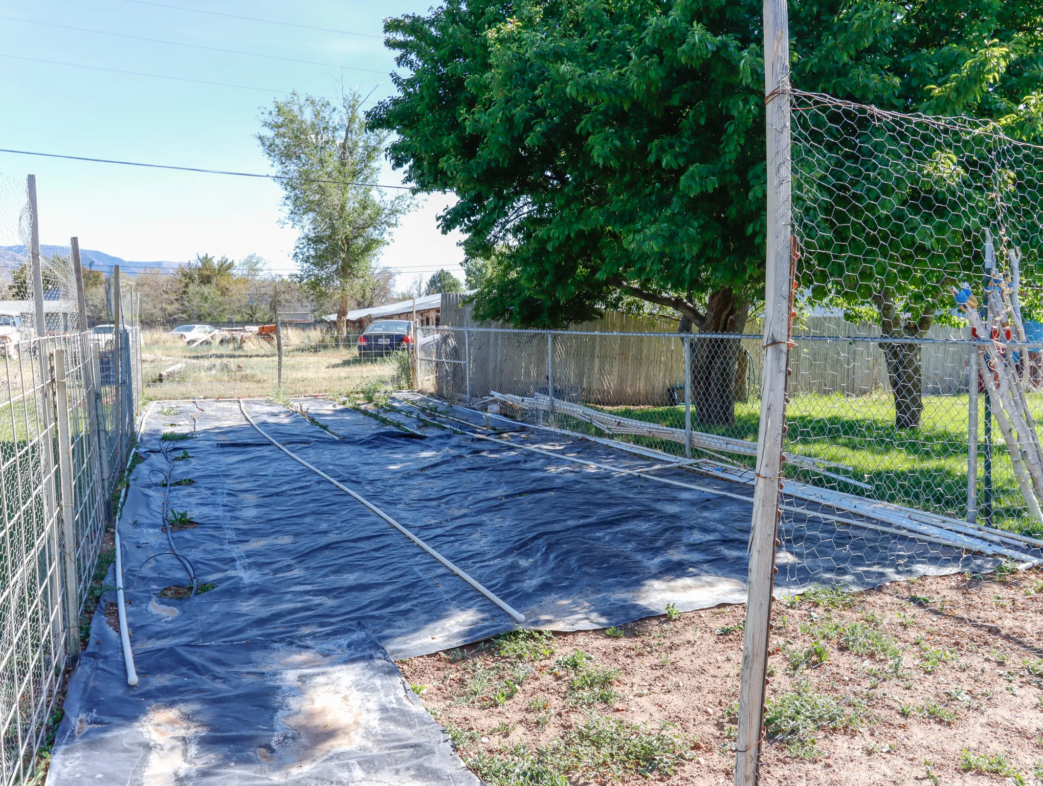Outdoor area featuring a dark ground covering, wire fencing, and mature trees