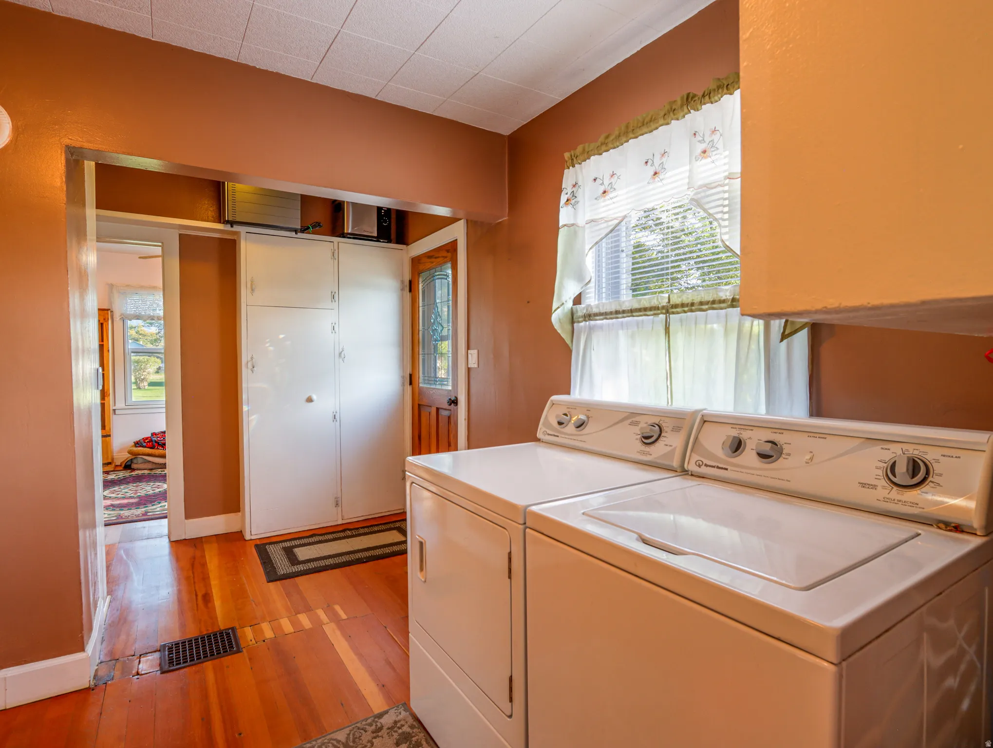 Laundry area featuring a window with blinds, a built-in cabinet for storage, and warm-toned wood flooring