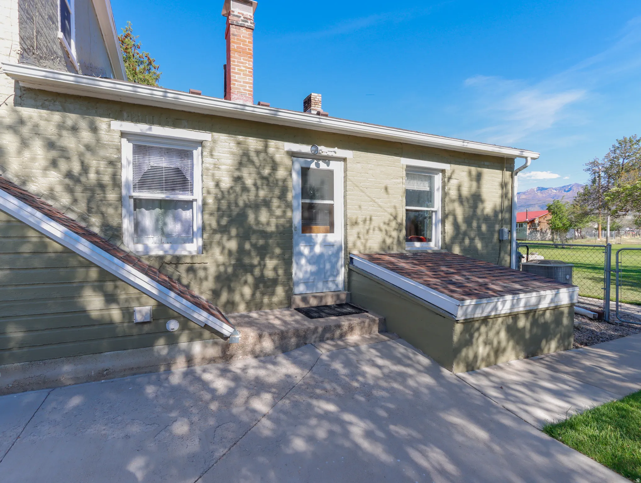 Exterior featuring light green siding, a white entry door, and multiple windows