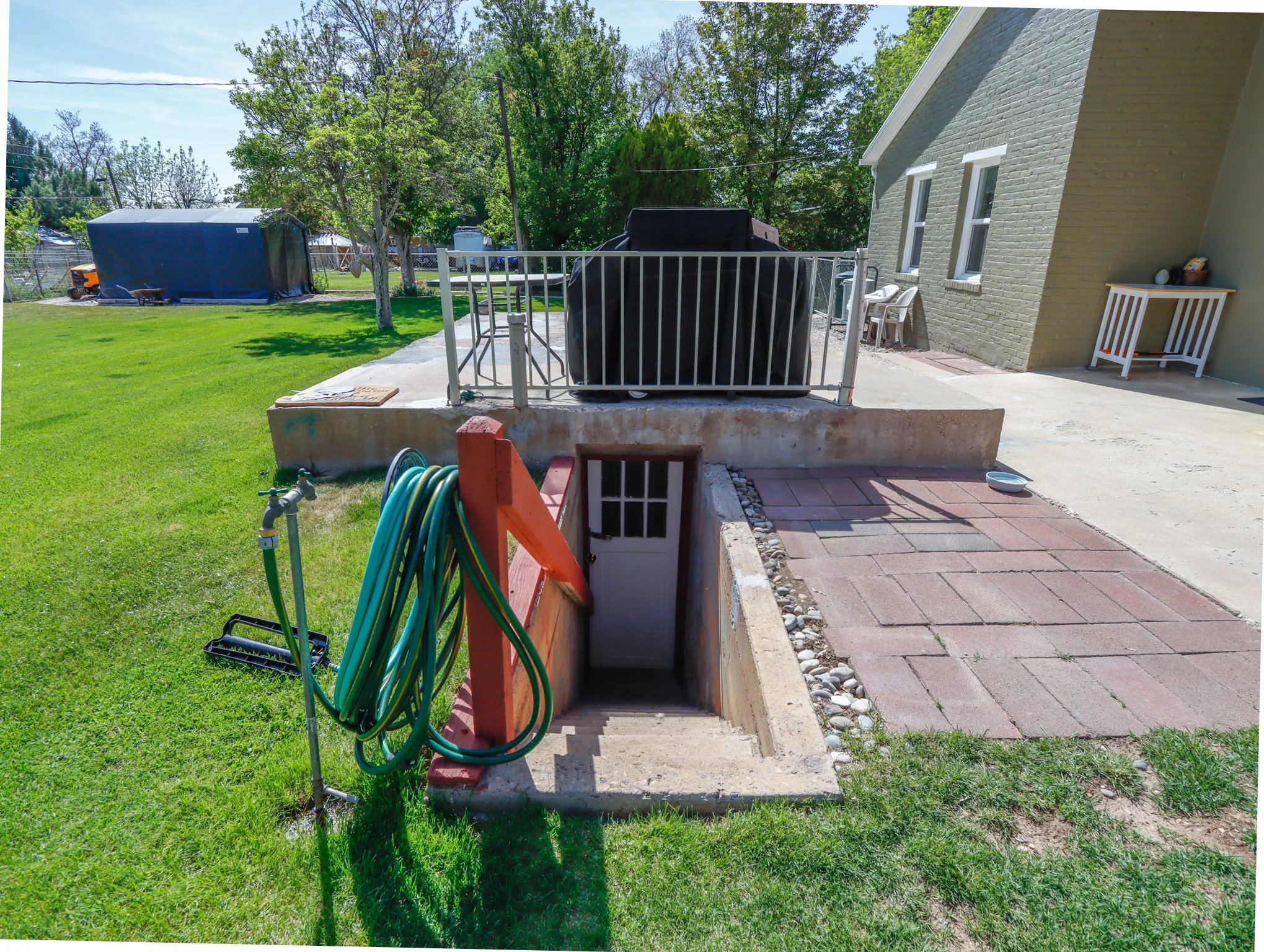 Exterior basement access featuring concrete steps, a white door, and a red-painted wooden railing