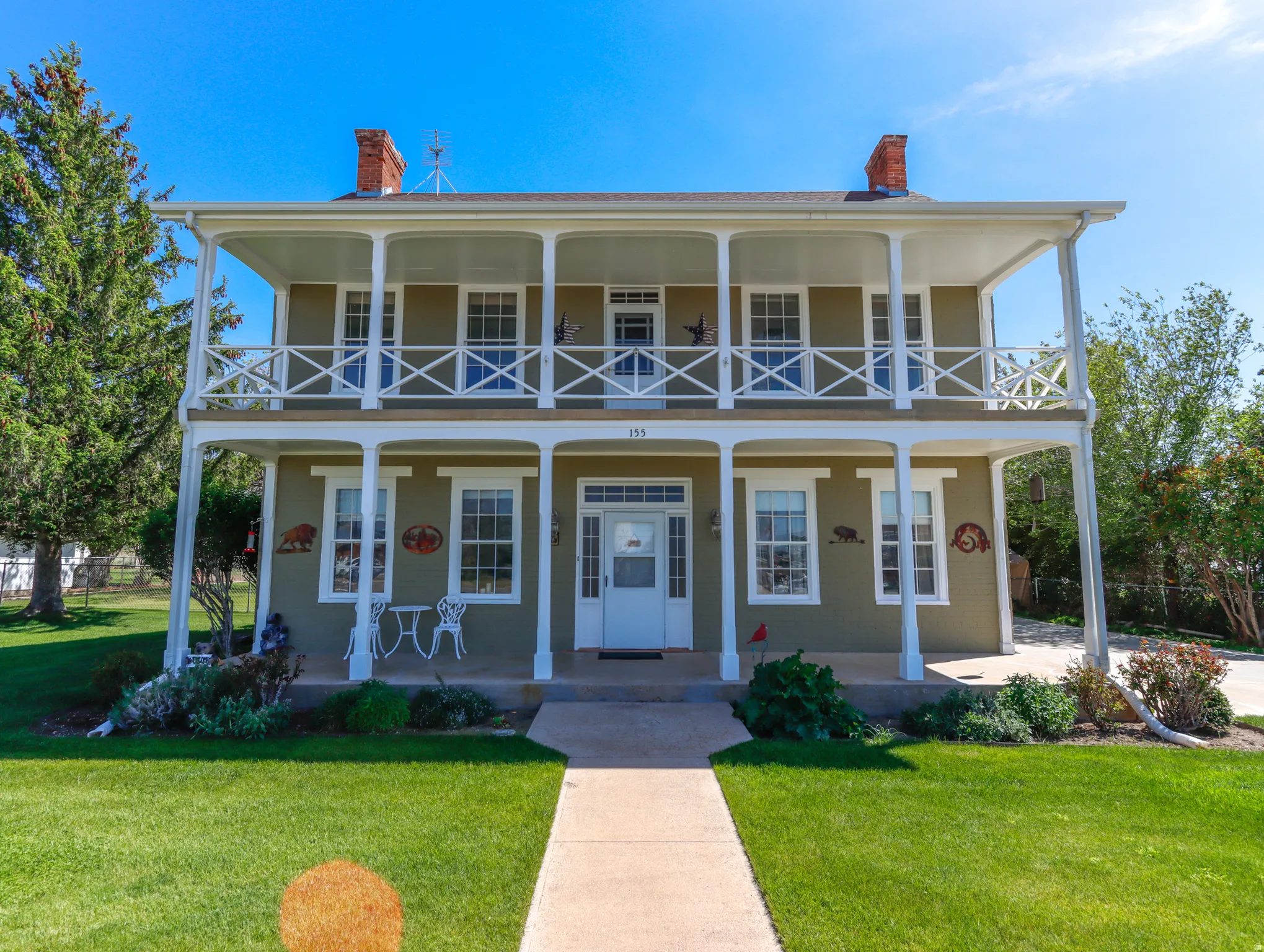 Two-story colonial-style facade featuring double-tier covered porches, white railings, and twin brick chimneys