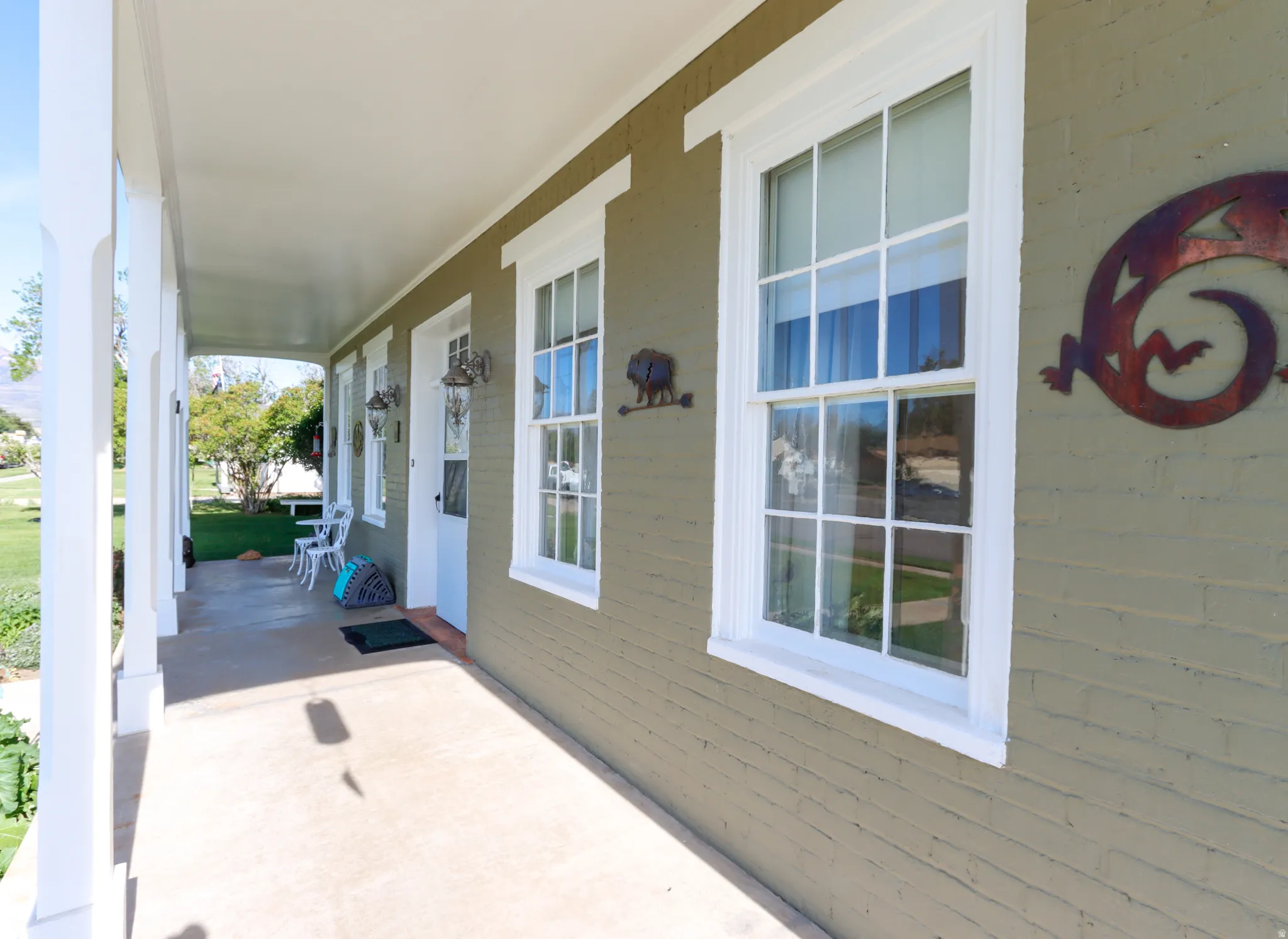 Covered front porch featuring a painted brick exterior, multiple double-hung windows with white trim, and a white front door
